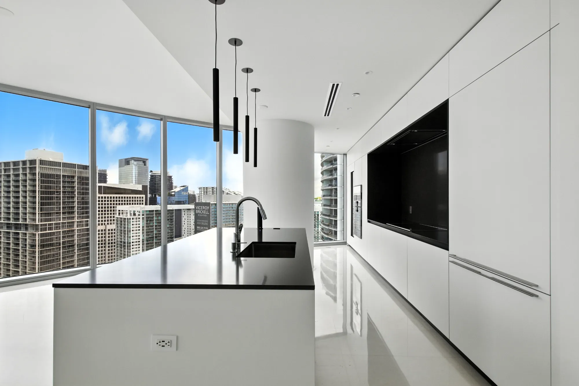 Luxury kitchen with a city view at Aston Martin Residences in Miami. Pendant lights hanging over the kitchen island and round support column off the side of the kitchen.